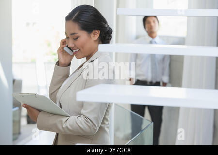 Estate agent talking on phone with buyer in background Stock Photo