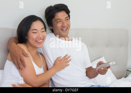 Smiling asian couple lying on bed watching tv Stock Photo