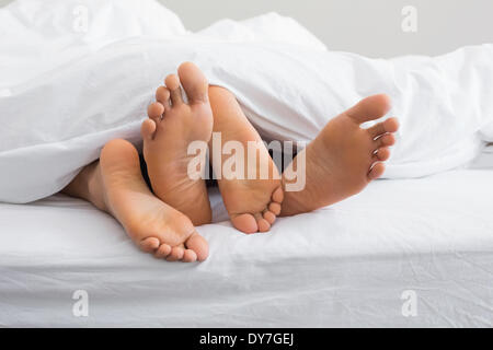 Couples feet sticking out from under duvet Stock Photo