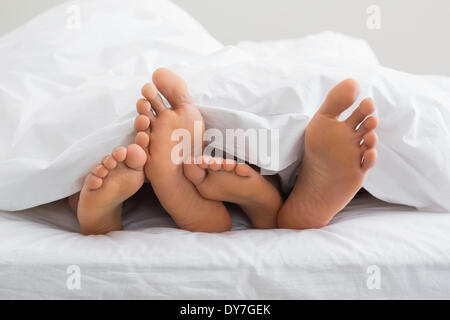 Couples feet sticking out from under duvet Stock Photo