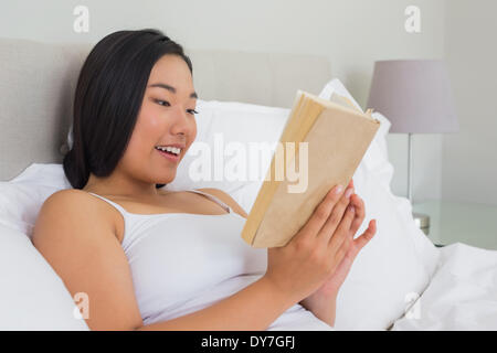 Smiling woman lying on bed reading Stock Photo