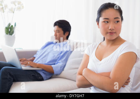 Upset woman sitting on couch while boyfriend uses laptop Stock Photo