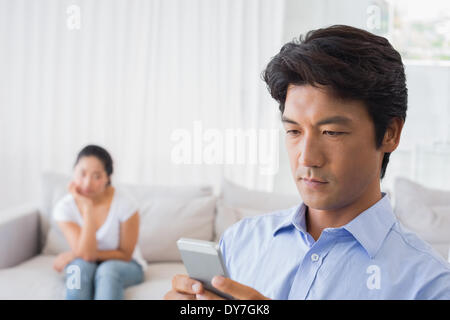 Man sending a text while girlfriend watches from couch Stock Photo