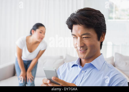 Man sending a text while girlfriend watches from couch Stock Photo