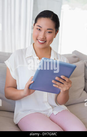 Smiling woman sitting on couch using tablet pc Stock Photo