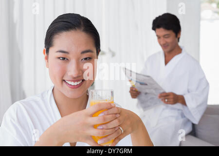 Woman in bathrobe having orange juice with boyfriend in background