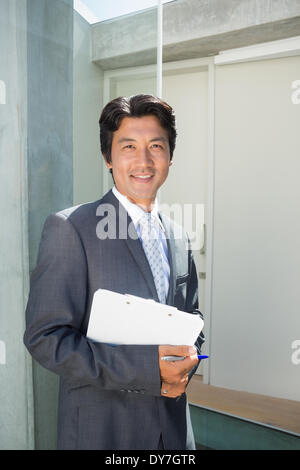 Confident estate agent standing at front door with clipboard Stock Photo
