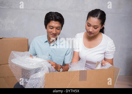 Happy couple sitting on floor unpacking boxes Stock Photo