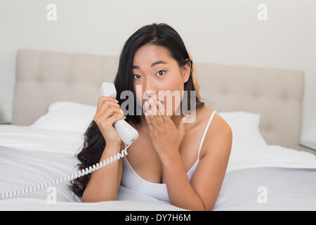 Shocked woman lying on bed holding telephone Stock Photo