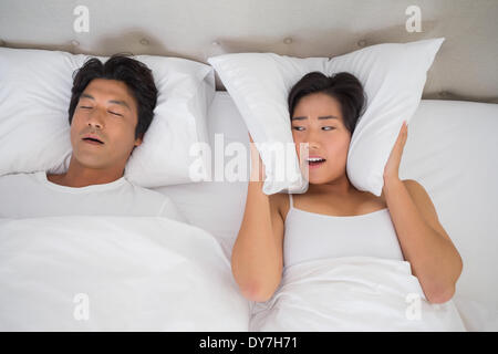 Annoyed woman covering her ears with pillows to block out snoring Stock Photo