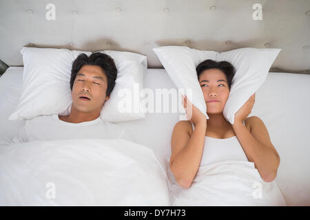 Annoyed woman covering her ears with pillows to block out snoring Stock Photo