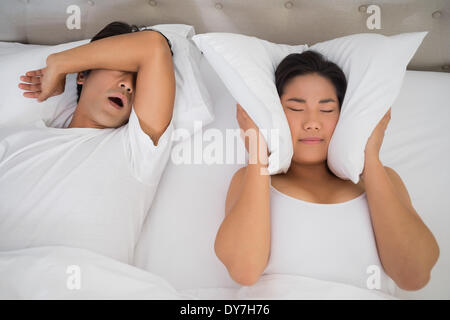Annoyed woman covering her ears with pillows to block out snoring Stock Photo