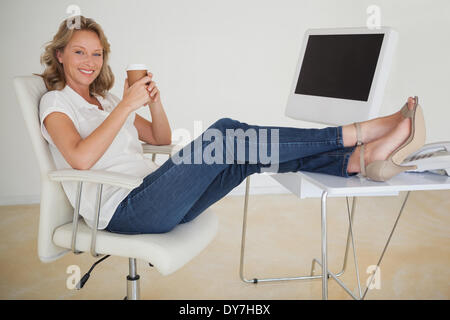 Casual businesswoman having a coffee with her feet up at desk Stock Photo