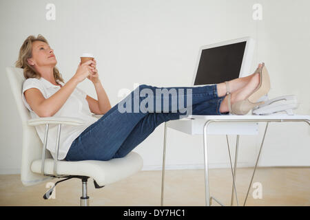 Casual businesswoman having a coffee with her feet up at desk Stock Photo