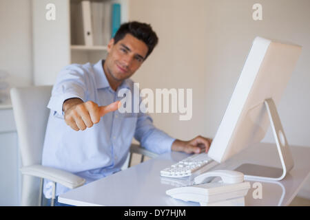 Casual businessman giving thumbs up to camera at his desk Stock Photo