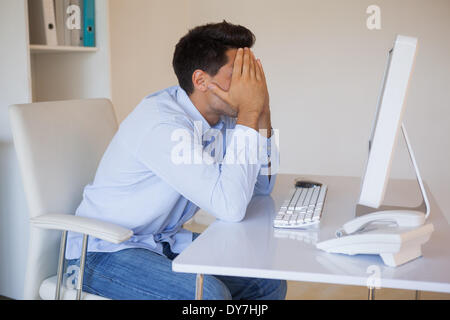 Casual businessman sitting at desk with head in hands Stock Photo