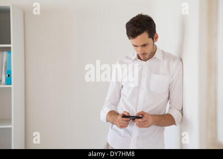 Casual businessman leaning against wall sending a text Stock Photo