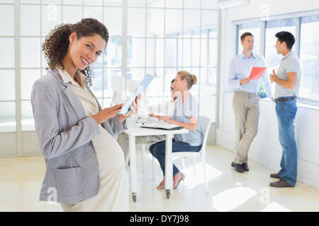 Pregnant businesswoman using tablet with team behind her Stock Photo