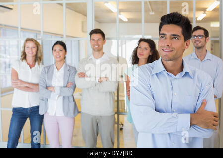 Casual boss smiling with arms crossed in front of business team