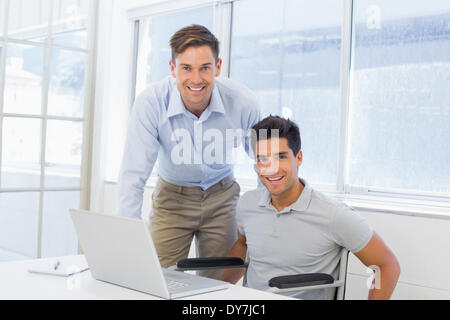 Casual businessman in wheelchair working at his desk with colleague Stock Photo