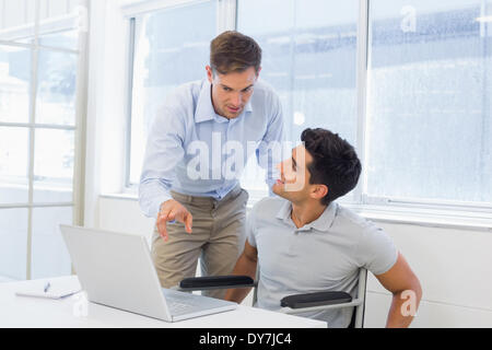 Casual businessman in wheelchair talking with colleague using laptop Stock Photo