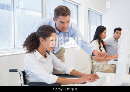 Casual businesswoman in wheelchair working at her desk with colleague Stock Photo