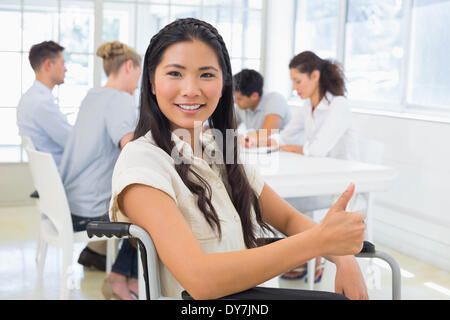 Casual businesswoman in wheelchair smiling at camera with team behind her