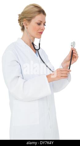 Blonde doctor in lab coat listening with stethoscope Stock Photo