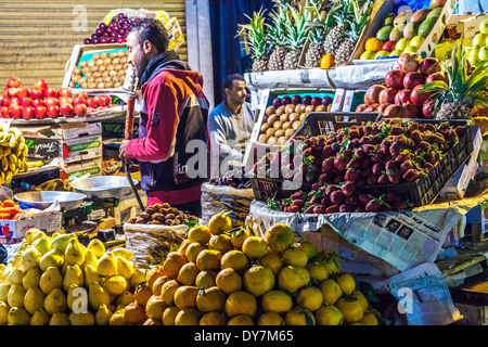 Stallkeeper smoking a hookah behind a fruit stall at the night market or souk in Luxor, Egypt Stock Photo