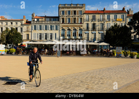 A mature woman cyclist passes pavement cafes. Rochefort. Charente-Maritime department of the Poitou-Charentes region of France. Stock Photo