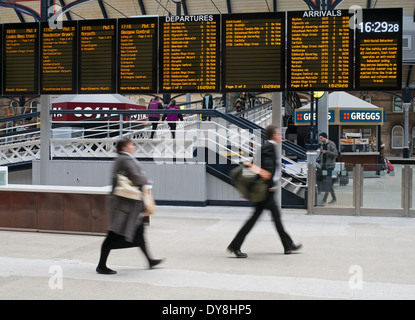 Blurred people hurrying to catch train below destination boards Newcastle upon Tyne station north east England UK Stock Photo