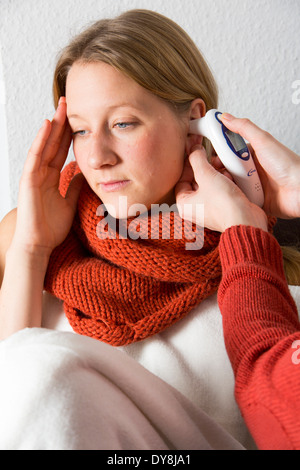 Young woman lying in bed, has a cold, fever, flu, fever, measured with a digital thermometer Stock Photo