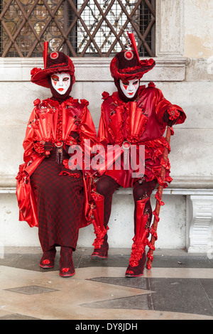 Sitting couple in red elegant historic costumes and masks during the Venice carnival Stock Photo