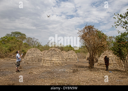 the past and the future: tourist flying a drone while a Mursi woman looks on, Mago National Park, Lower Omo, Ethiopia Stock Photo