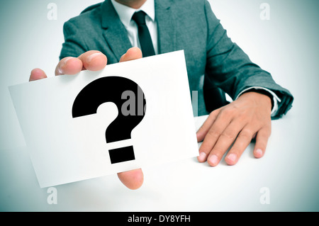 a man wearing a suit sitting in a desk holding a signboard with a question mark Stock Photo