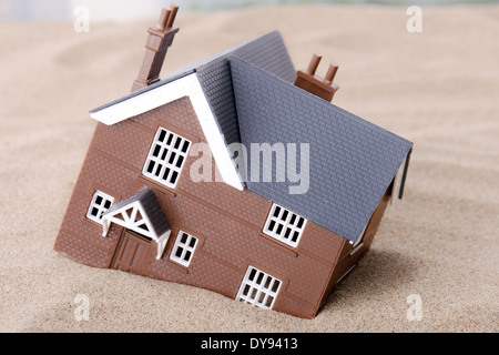 A house sinking in sand, concept for housing problems Stock Photo