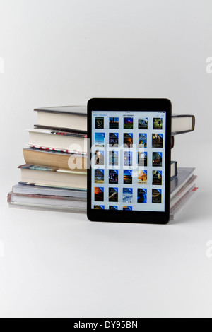 Apple iPad mini displaying icons for 28 books with a stack of only 6 printed paper books Stock Photo