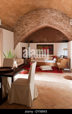 Open plan dining and living room with ancient stone arch. The dining chairs are covered in raw silk. Stock Photo