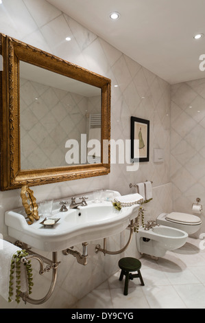 Gilt framed mirror in marble lined bathroom Stock Photo