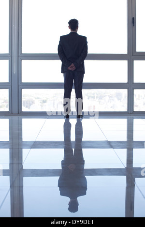 Businessman looking out high rise window at view of city below at sunset Stock Photo
