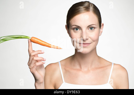 Young woman holding up raw carrot Stock Photo