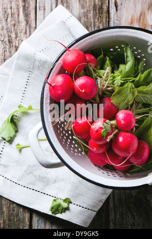 Top view on fresh wet radishes in white colander over old wooden table Stock Photo
