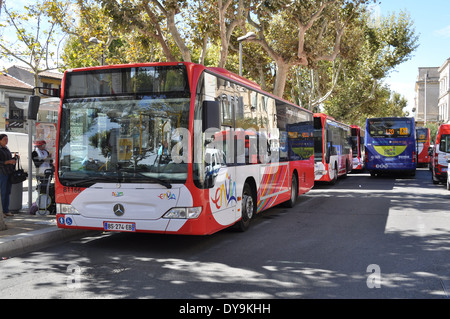 People waiting at bus stop and a line of urban passenger mass transport buses in the centre of town Arles France Stock Photo