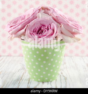 Pink roses in a green polkadot vase on vintage white wooden shabby chic background Stock Photo