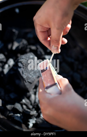 Striking a matchstick, burn up a charcoal in barbecue grill, prepare for cooking Stock Photo
