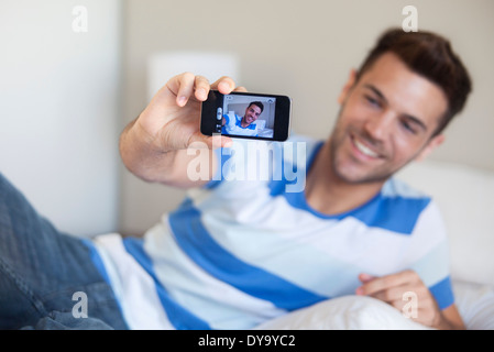 Young man reclining on bed taking selfie with smartphone Stock Photo