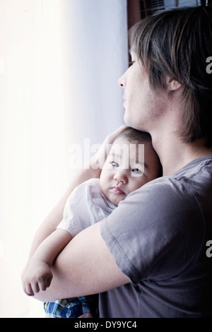 Father holding baby, looking out window Stock Photo