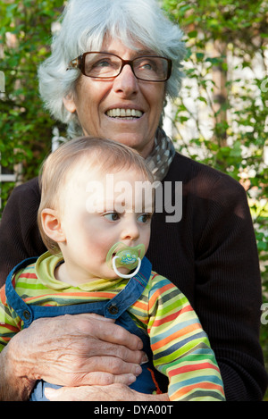 Grandmother holding young grandson on lap outdoors Stock Photo