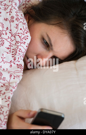 Woman lying bed looking at smartphone with unhappy expression on face Stock Photo