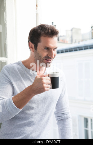 Man looking out of window with mug in hand Stock Photo